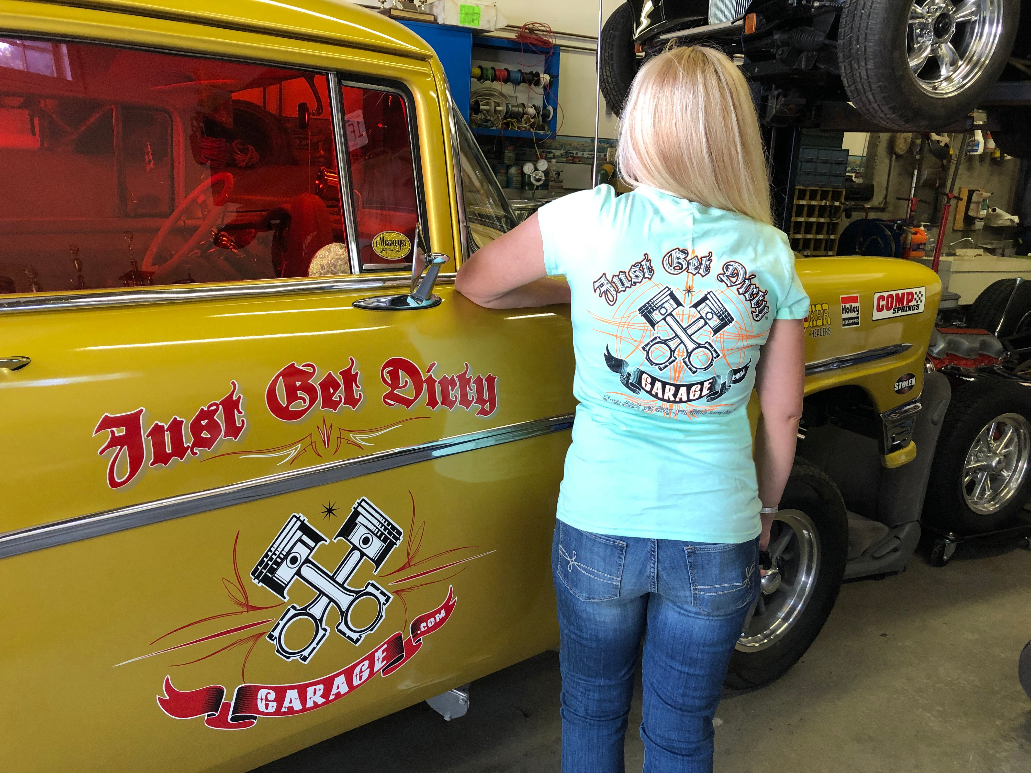 Person wearing a 'Just Get Dirty Garage' t-shirt standing next to a yellow car in a garage.